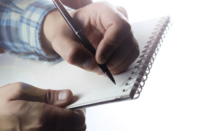 A person writing on a pad of paper with a pen